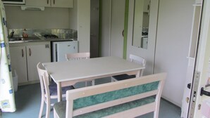 A compact kitchen with a dining area, including a table and chairs, a small refrigerator, and a microwave. - Camping des Etoiles - Chalets (Najac)