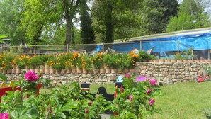 A garden with a stone wall, wooden planters with flowers, and a blue tarp-covered structure. - Camping des Etoiles - Chalets (Najac)