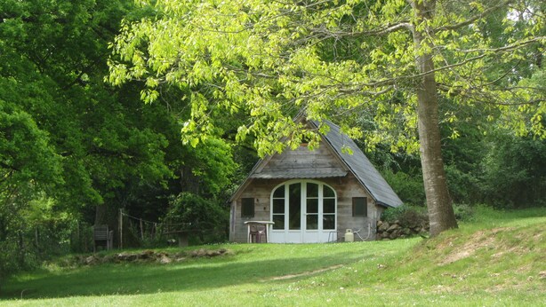 A small wooden cabin with a sloped roof, surrounded by lush green trees and a grassy area. - Camping des Etoiles - Chalets (Najac)