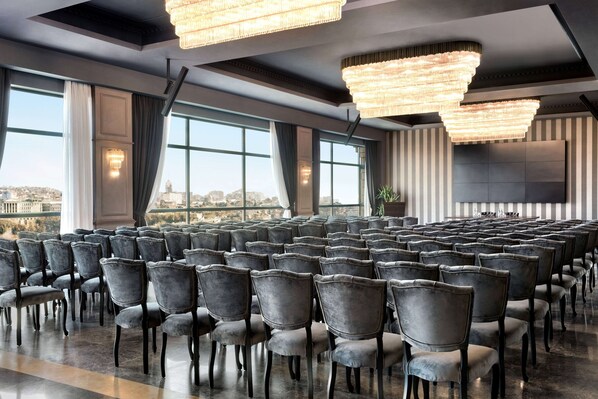 A conference room with rows of chairs, large windows, and chandeliers. - Wyndham Grand Tbilisi (Tbilisi)