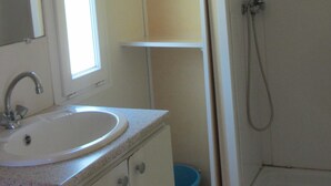 A bathroom with a sink, mirror, shelves, and a shower. - Camping des Etoiles - Mobil-Home (Najac)
