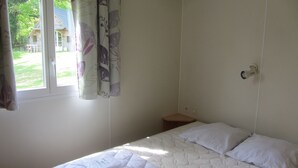 A small, simple room with a bed, a window, and a small table. - Camping des Etoiles - Mobil-Home (Najac)