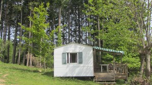 A small cabin with a porch and a table, surrounded by a forest. - Camping des Etoiles - Mobil-Home (Najac)