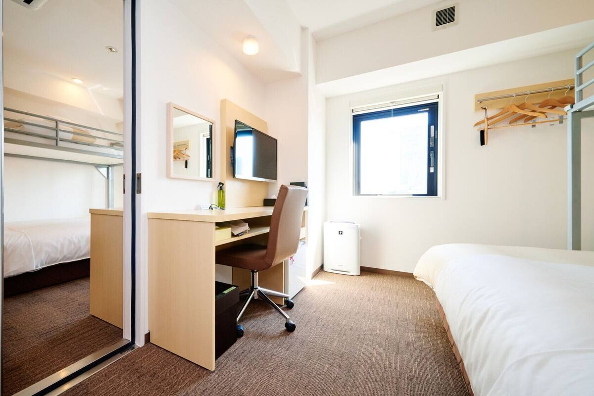 Une chambre d’hôtel avec un lit superposé, un bureau, une chaise et une fenêtre.