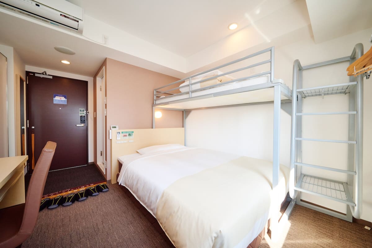 Une chambre d’hôtel avec un lit superposé, un bureau avec une chaise, un porte-chaussures et une porte avec une pancarte.