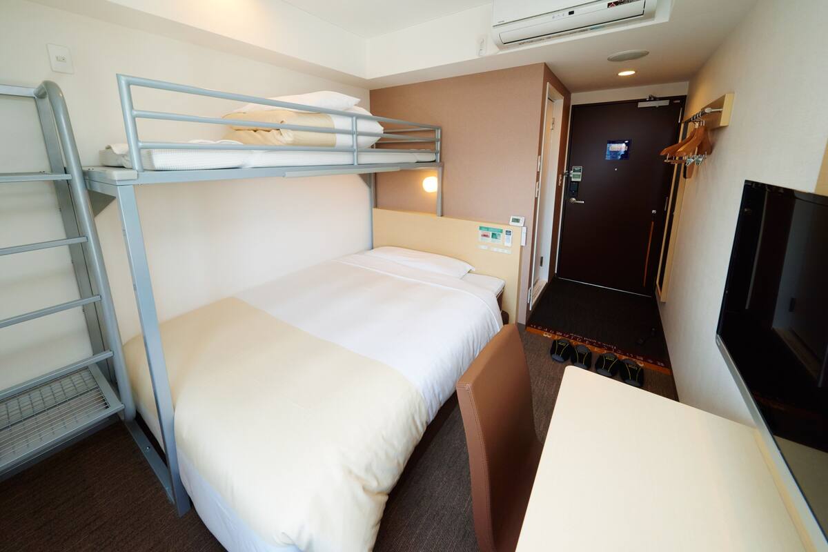 Une chambre avec un lit superposé, un bureau et une télévision.