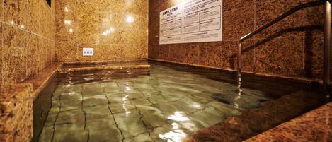 A hot spring bath area with tiled walls and a sign providing information about the water's carbonated content.