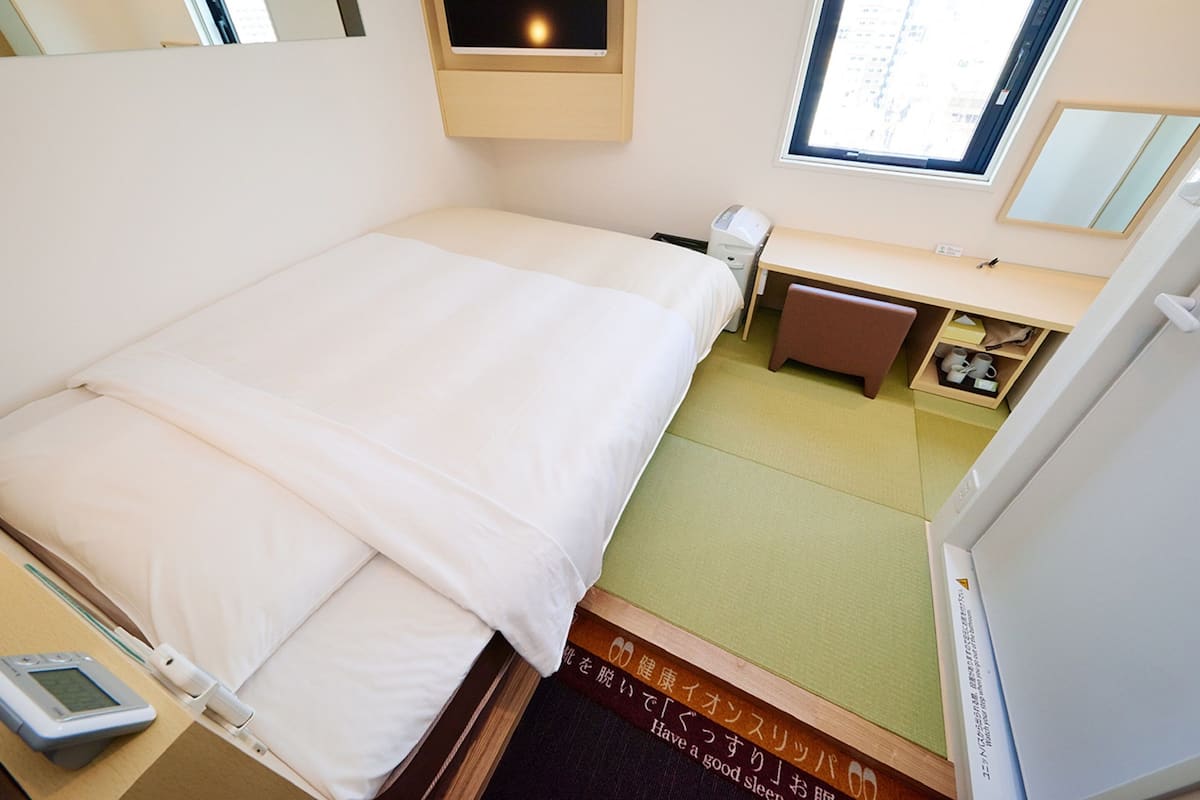 Une chambre d’hôtel comprenant un lit, une table de chevet, un bureau, une chaise et une fenêtre.