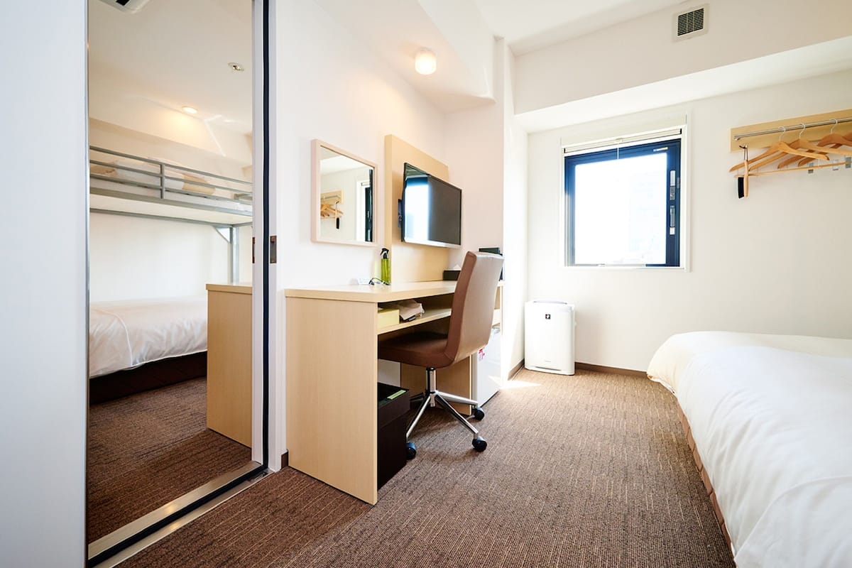 Une chambre d’hôtel avec un lit superposé, un bureau avec une chaise, une télévision et une fenêtre donnant sur un paysage agréable.