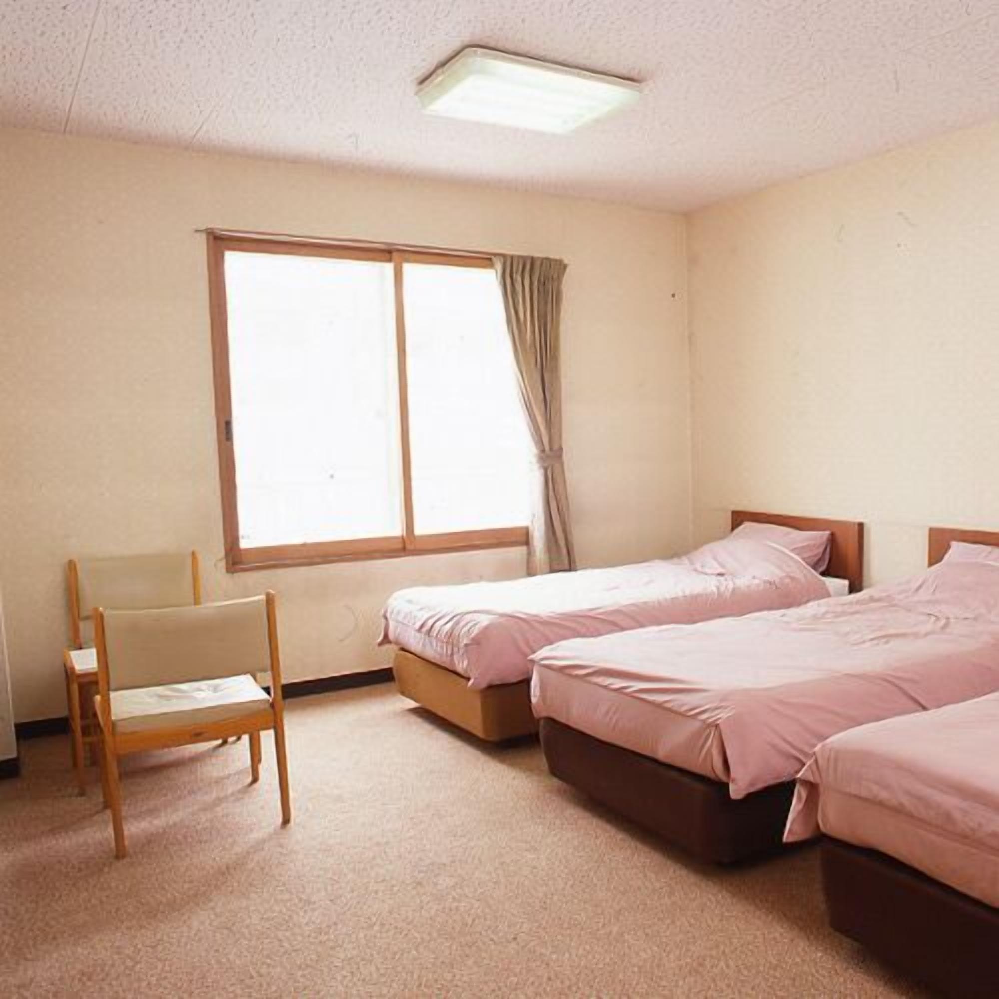 Un dormitorio con dos camas, una silla y una ventana.