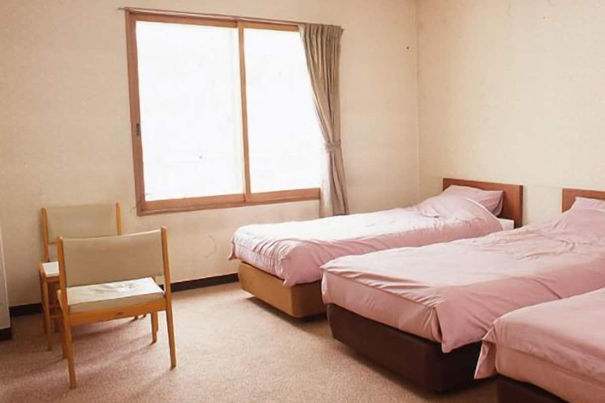 A bedroom with two beds, a chair, and a window.