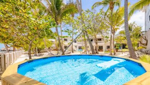 A hot tub surrounded by palm trees and a pool, with a building in the background. - Babylon Beach (San Pedro)