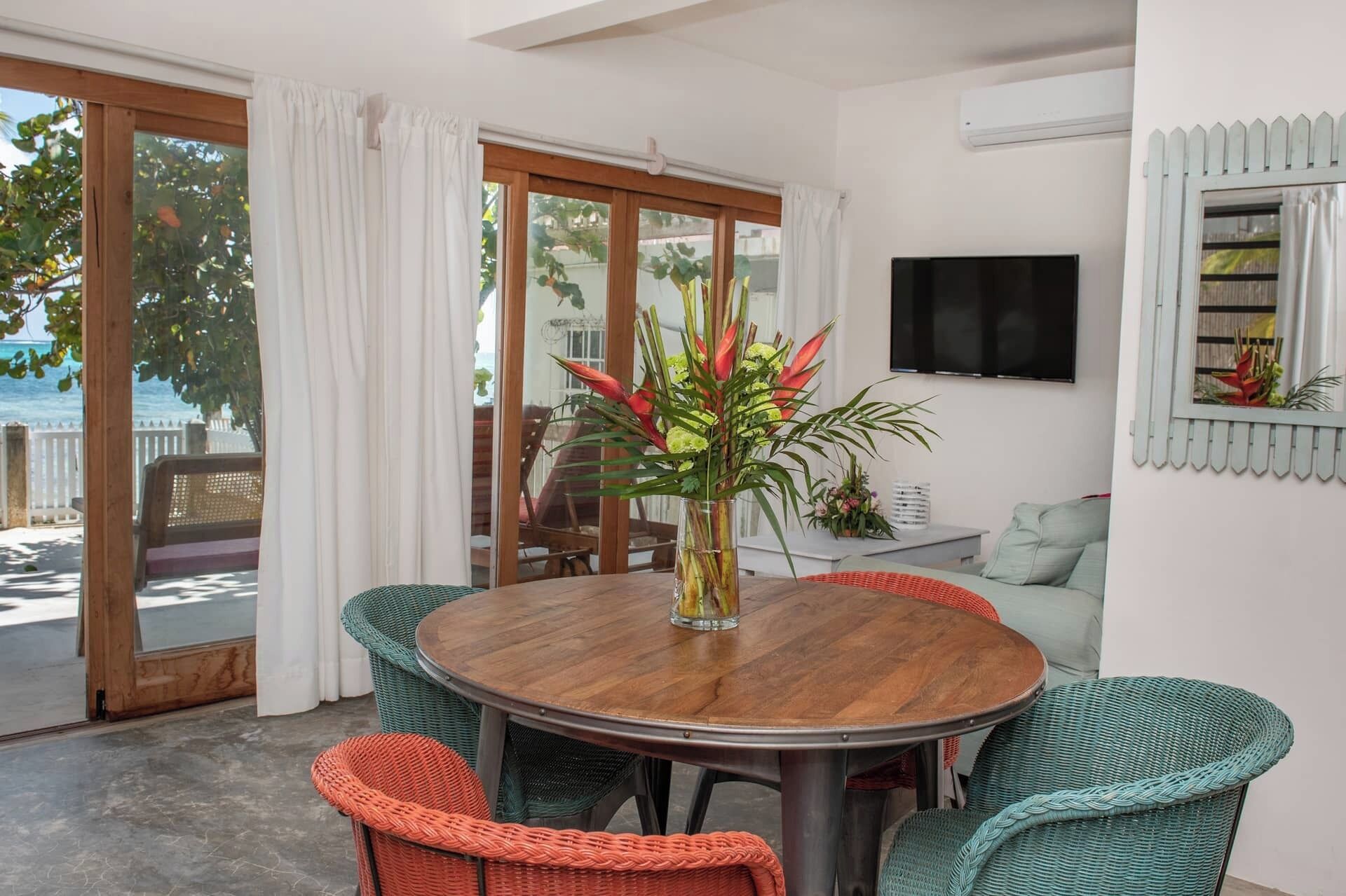 A dining area with a round wooden table, wicker chairs, and a view of the outdoors through large sliding glass doors.