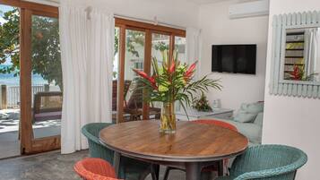 A dining area with a round wooden table, wicker chairs, and a view of the outdoors through large sliding glass doors.