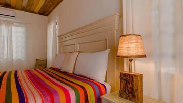 A bed with a colorful striped blanket, a wooden nightstand with a lamp, and a white headboard.