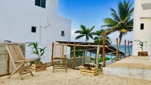 A rooftop terrace with a wooden pergola, two wooden chairs, a wooden crate with plants, and a view of the sea. - Beautiful Suite double beach front (Cancun)