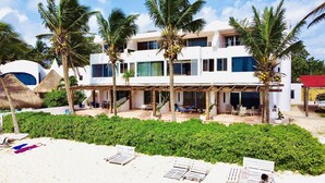 A modern two-story building with a covered patio area, surrounded by lush greenery and palm trees. - Beautiful Suite double beach front (Cancun)