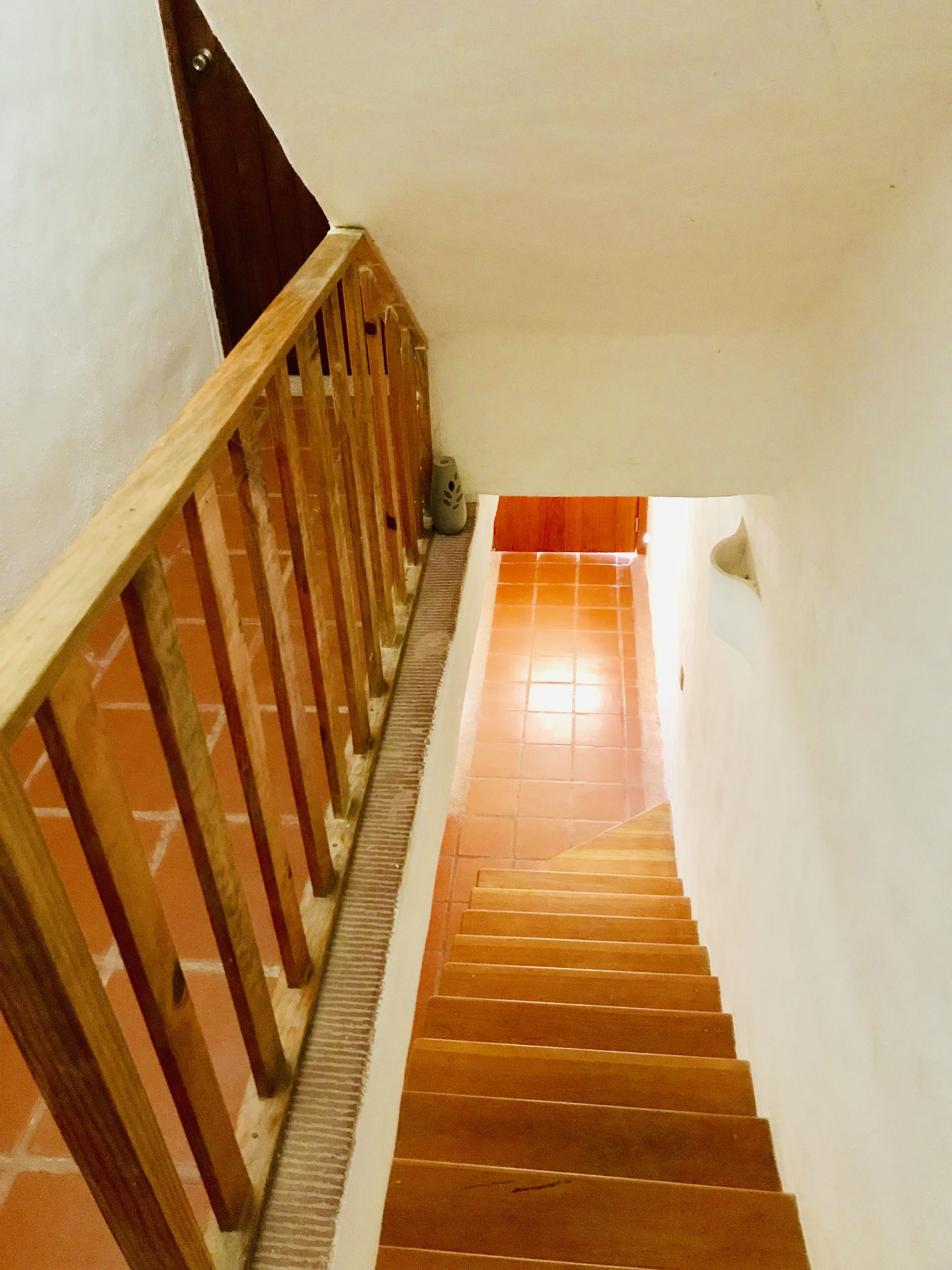A wooden staircase with a handrail, leading to a landing with a tiled floor.