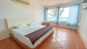 Un dormitorio con cama, mesita de noche, ventana con cortinas y vista al mar.