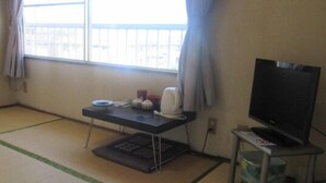 A room with tatami flooring, a low table with a television and remote, and a window with curtains. - Business Hotel New Ozai (Oita)