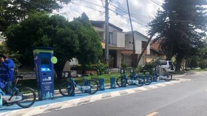 A street with a bike parking area, a blue kiosk, and a row of bicycles.