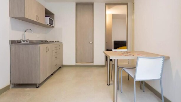 A compact kitchen with a microwave, sink, and cabinets, a small dining table with chairs, and a door leading to another room.
