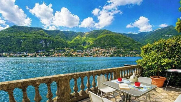 Eine Terrasse mit Blick auf einen See und Berge, Sitzgelegenheiten im Freien und ein Tisch mit einem Buch und roten Schüsseln.