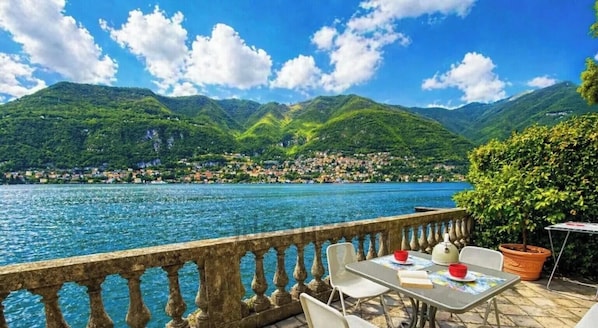 A terrace with a view of a lake and mountains, outdoor seating, and a table with a book and red bowls.