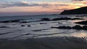 Uma praia com águas calmas, céu claro e paisagens distantes.