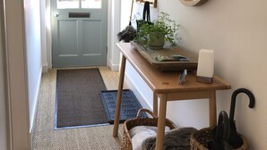 Um corredor com uma porta cinza, um console de madeira com uma planta, um espelho e uma cesta de vime.