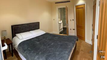 A bedroom with a large bed, a bedside table, a lamp, and a door leading to a bathroom.