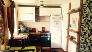 A compact kitchen with a microwave, kettle, and refrigerator, wooden cabinets, and a dining area with a table and chairs.