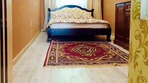 A bedroom with a bed, a large rug, a window with curtains, and a door.