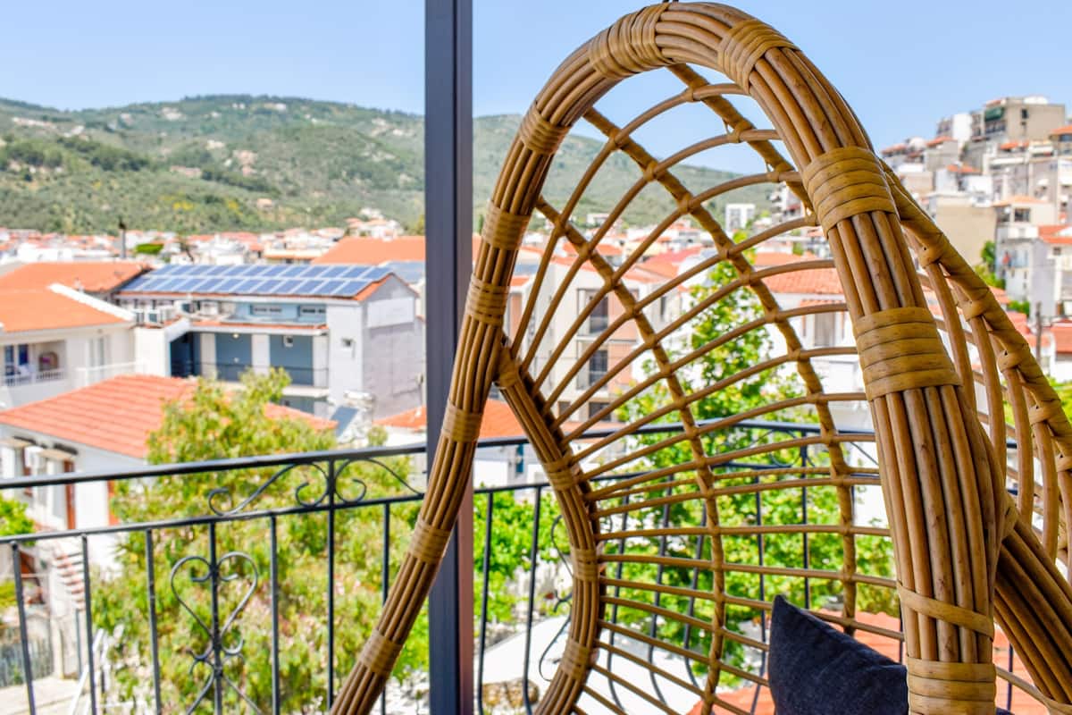A wicker chair with a view of a town with red-roofed buildings and greenery in the background.