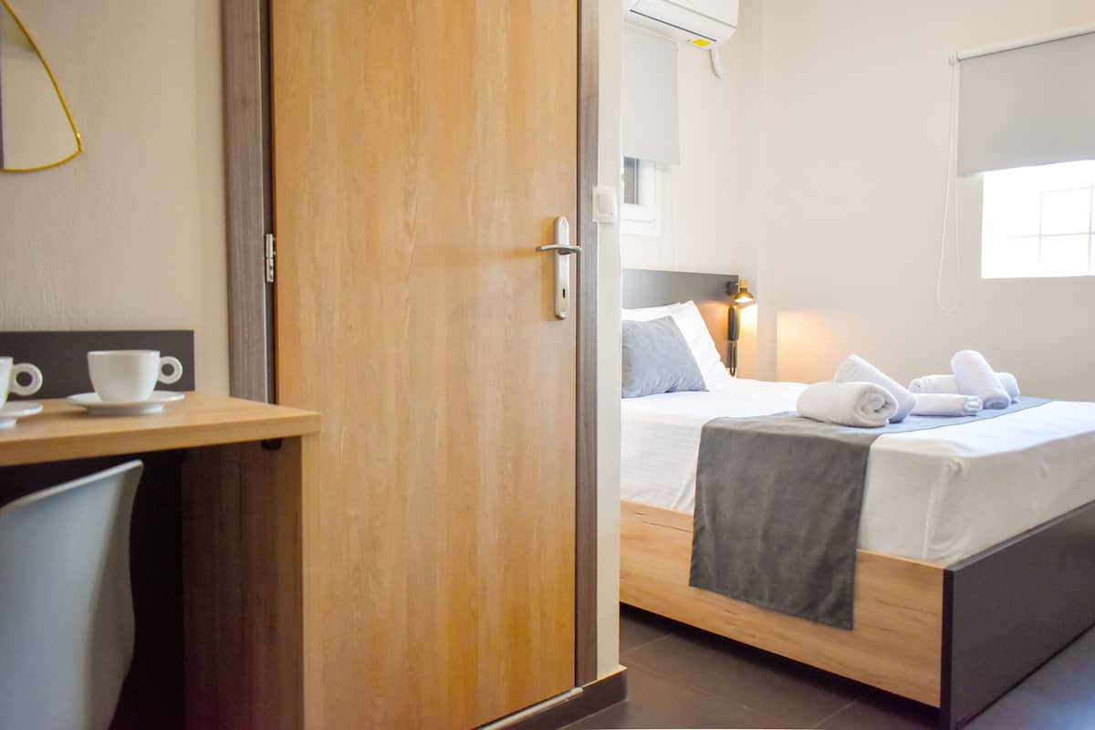 A hotel room with a wooden bed, a bedside table with a cup and saucer, and a window with blinds.