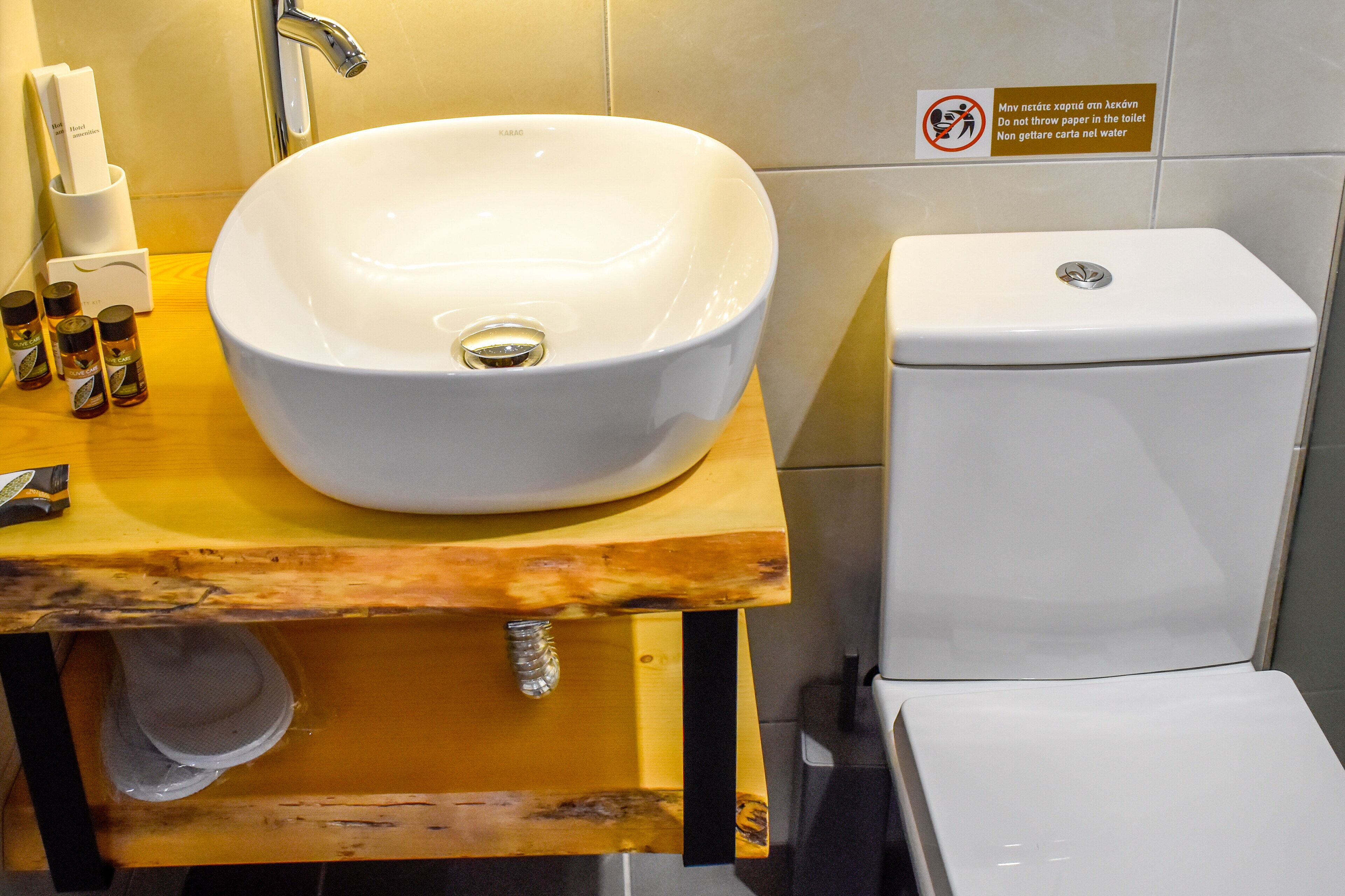 A bathroom with a white sink on a wooden vanity, a toilet, and a sign with instructions in a foreign language.