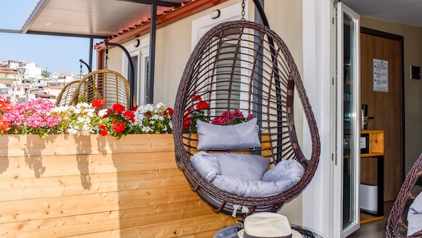 A wicker hanging chair with cushions, a wooden planter with flowers, and a hat on a table.