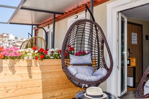 A wicker hanging chair with cushions, a wooden planter with flowers, and a hat on a table. - Entelia (Skiathos)
