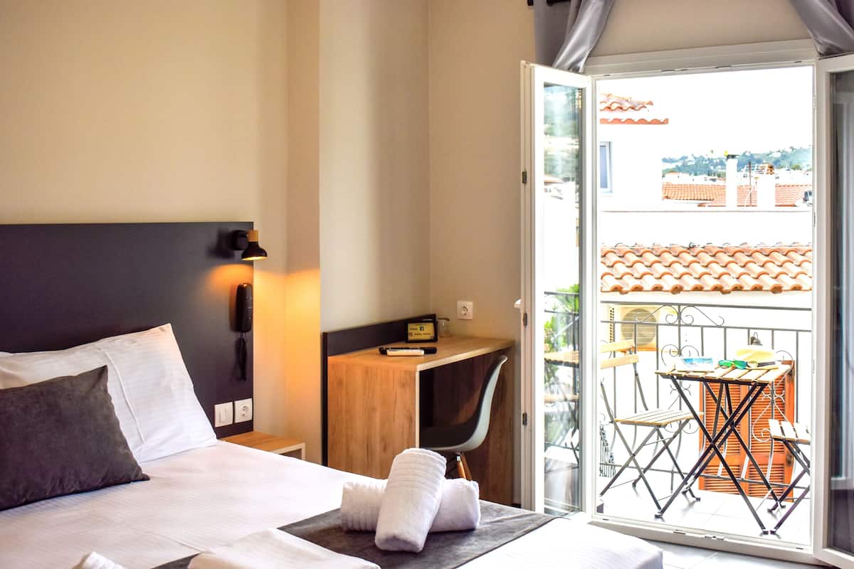 A hotel room with a bed, a desk, and a balcony with a table and chairs.