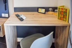 Una pequeña mesa de madera con un control remoto, un reloj digital pequeño y una tarjeta de menú.