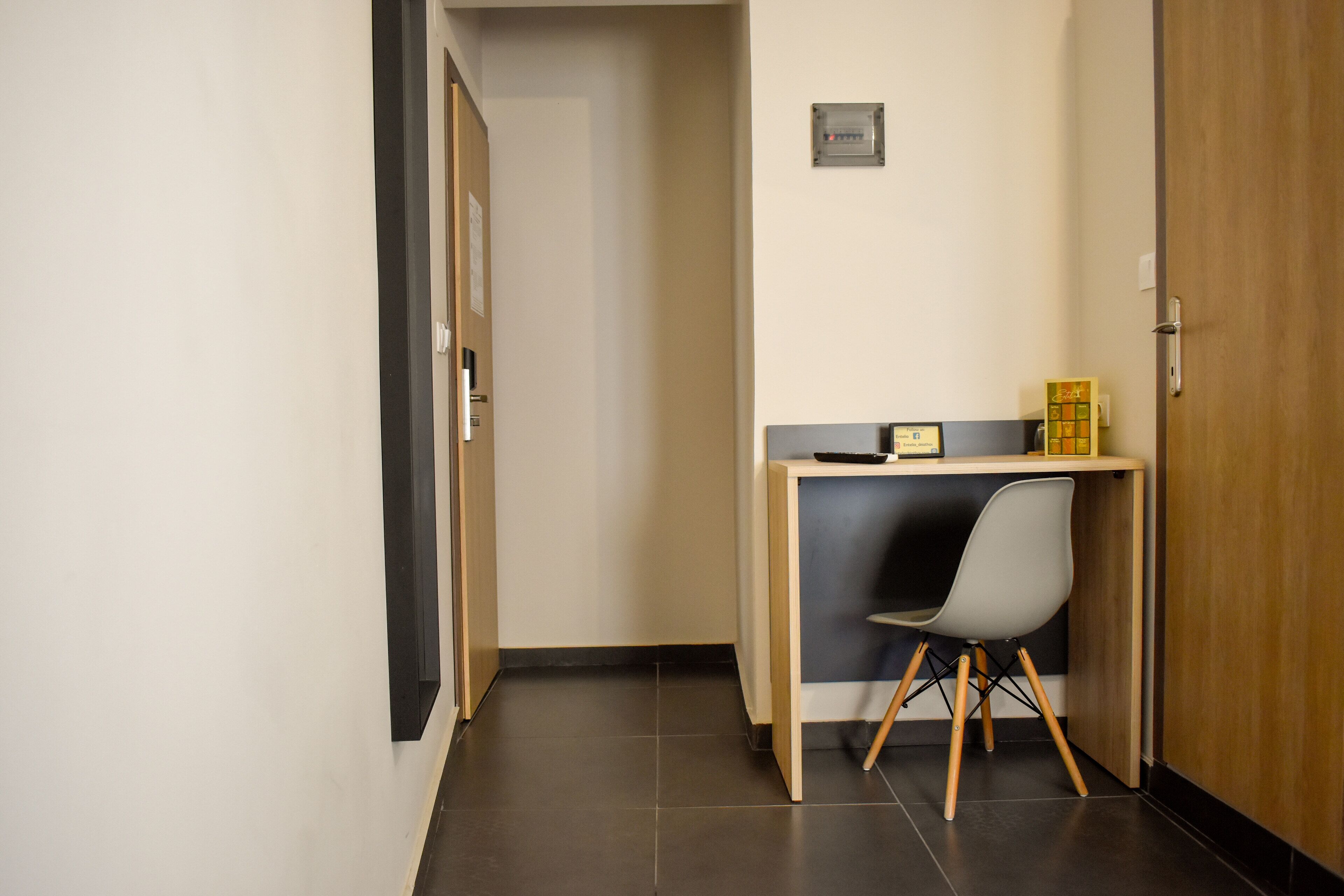 A small, narrow hallway with a desk and chair, a door, and a light switch on the wall.