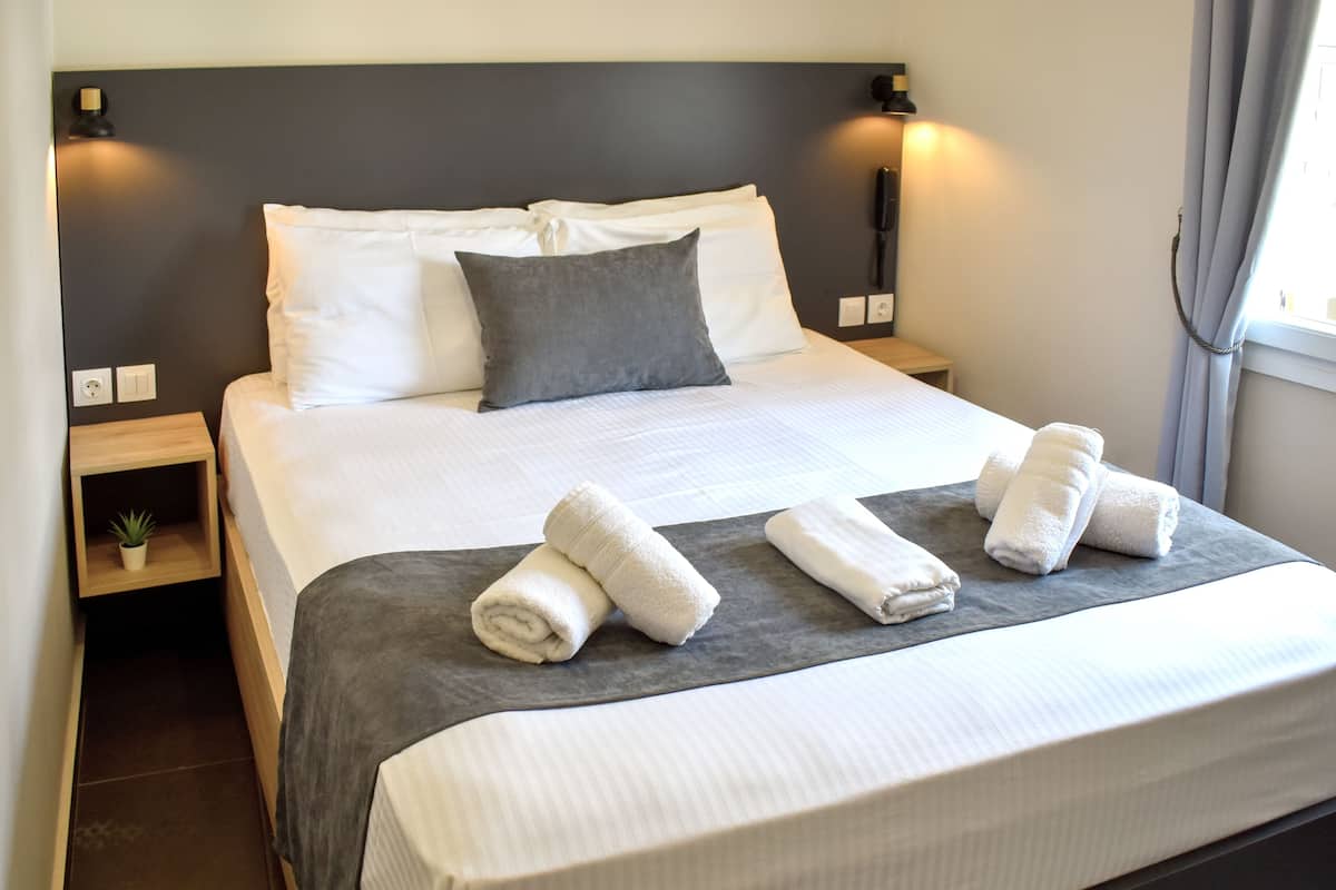 A neatly made bed with white and gray linens, two bedside tables with lamps, and a small plant on one table.