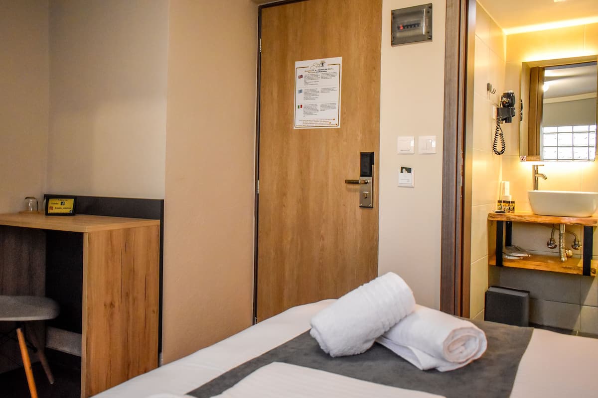 A hotel room with a bed, a wooden desk, a bathroom with a sink and mirror, and a door with a notice.