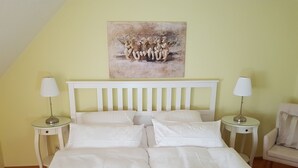 Ein Schlafzimmer mit einem weißen Bett, zwei Nachttischen, einem weißen Stuhl und einem Gemälde an der Wand.
