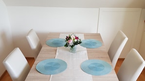 Ein Esstisch mit floraler Dekoration, vier blauen Platzsets und weißen Stühlen.