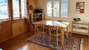 A wooden interior with a dining table, chairs, a TV, and a bookshelf. - Apartment Iris by Interhome (Lenk)