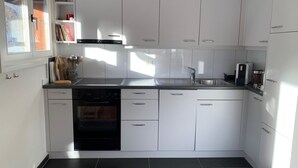 A modern kitchen with white cabinets, a dishwasher, an oven, and a sink. - Apartment Iris by Interhome (Lenk)