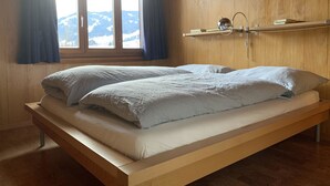 A single bed with a wooden frame and a view of mountains through a window. - Apartment Iris by Interhome (Lenk)