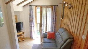 A cozy living room with a grey sofa, a television on a wooden stand, and a window with curtains. - Heiderösli by Interhome (Grächen)