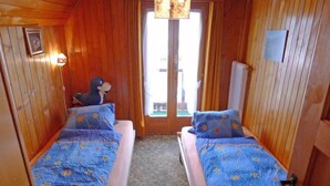 A room with two beds, wooden walls, a window, and a wall-mounted TV. - Heiderösli by Interhome (Grächen)